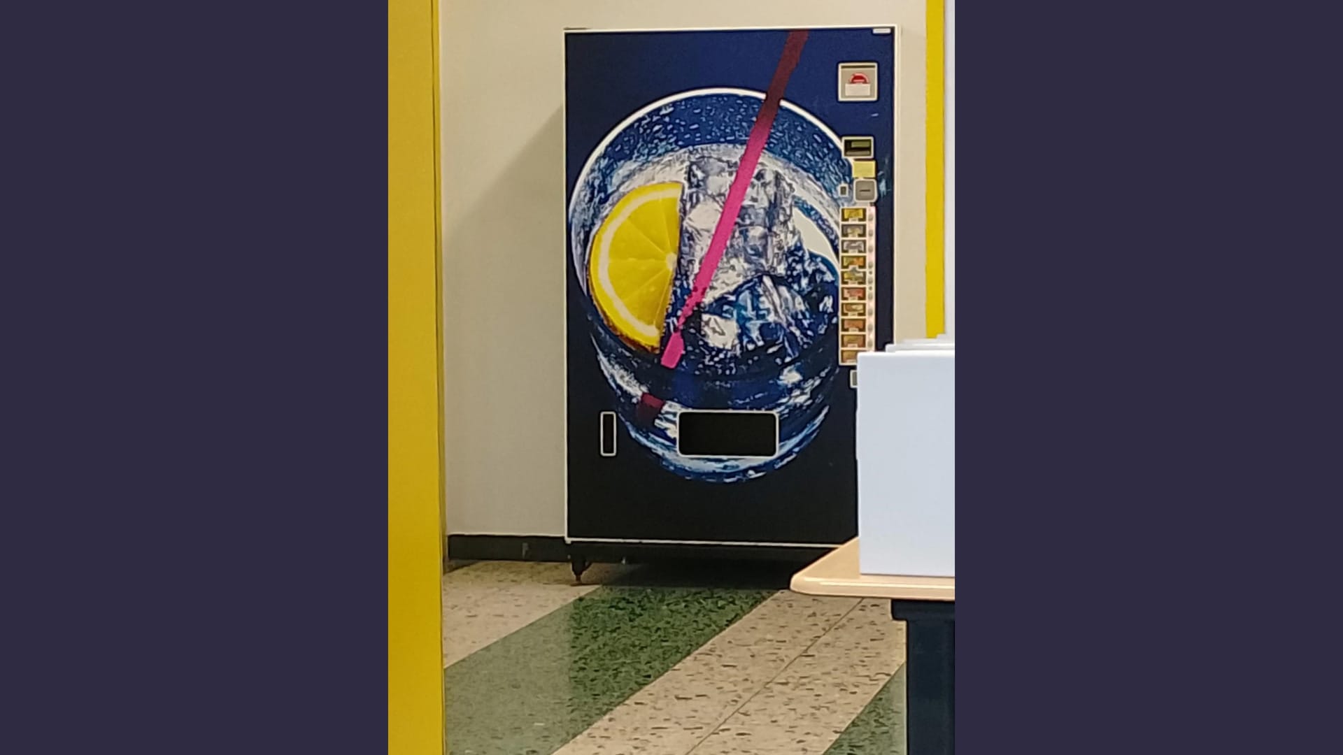 Foto: Ein Getränkeautomat, auf den ein großes Glas mit Eiswürfeln und einer quietschgelben Zitrone aufgemalt ist