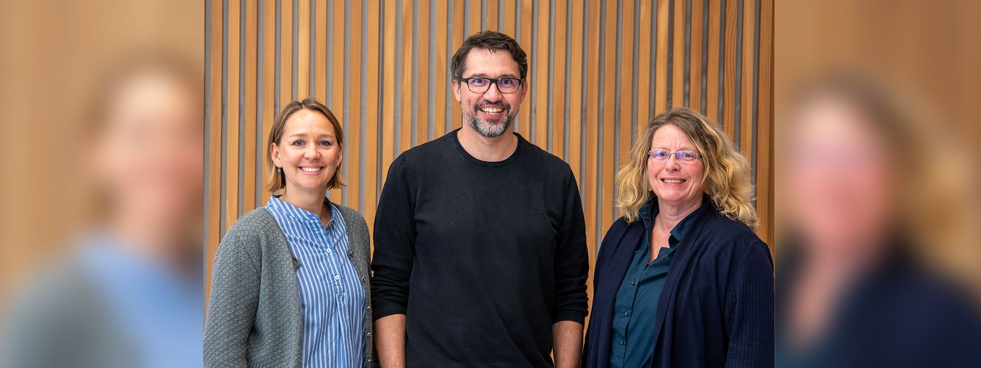 Foto: Drei Erwachsene (zwei Frauen und ein Mann) lachen freundlich in die Kamera