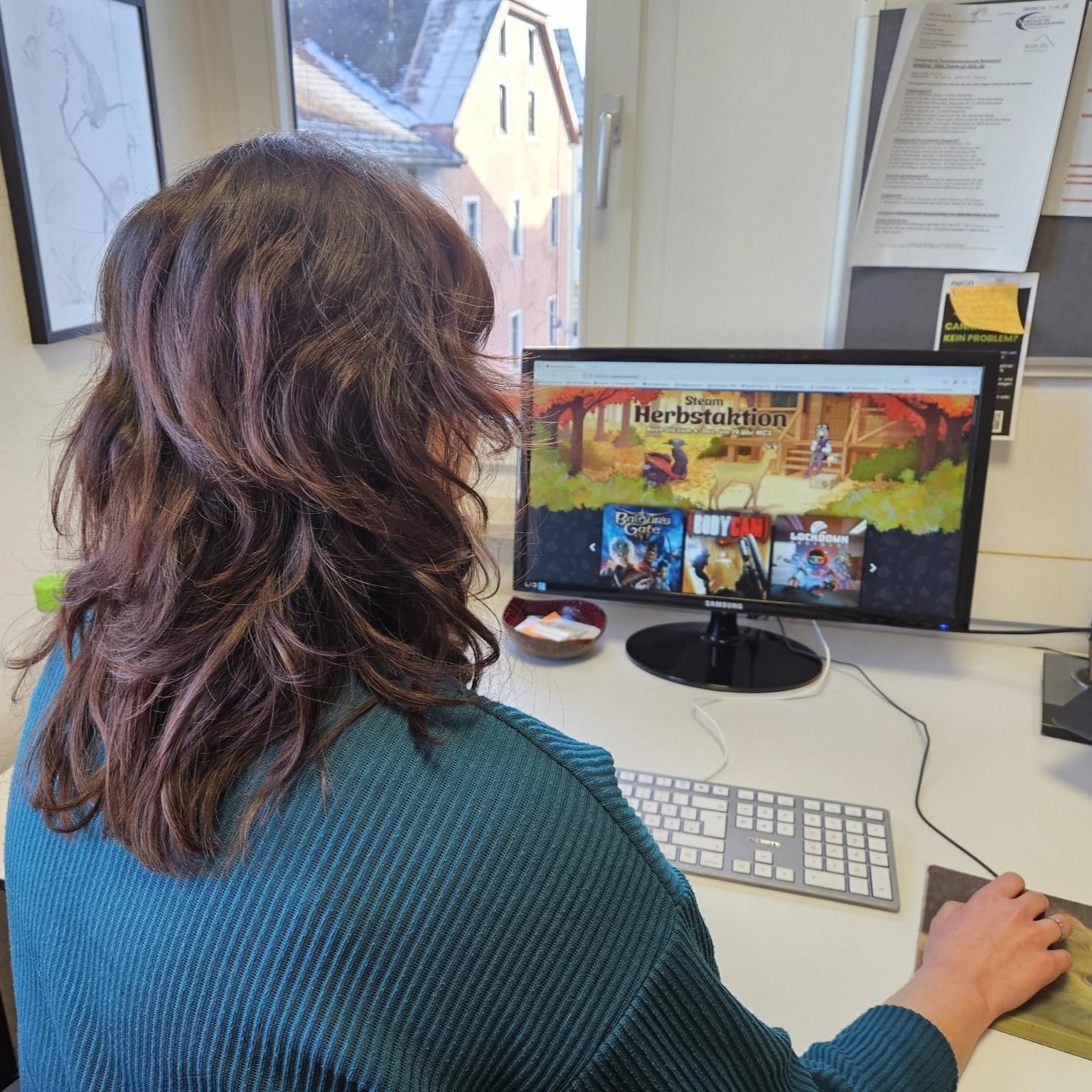 Foto: Adelina vor dem Bildschirm ihres Arbeits PCs, wo man Thumbnails von ein paar Games sieht