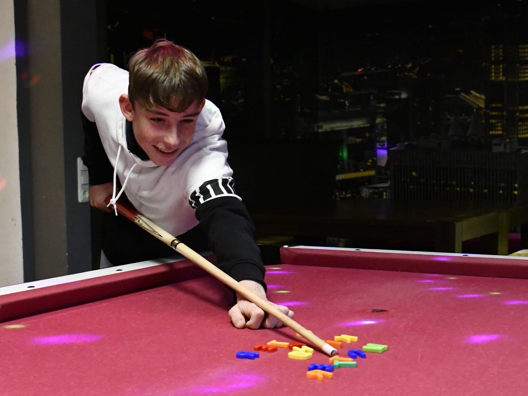 Foto: Ein Jugendlicher hat Spaß daran, mit einem Billard-Queue Magnetbuchstaden durcheinanderzustoßen, die die Worte Vater, Mutter, Kind gebildet hatten