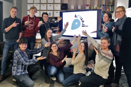 Gruppenfoto mit sechs aROund-Redakteuren, Anne, Hanna, Frederic und Erik, die auf einen Bildschirm zeigen, auf dem das aROund-Logo abgebildet ist.