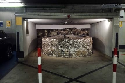 Foto einer Brunnenruine, die überdacht wurde und um die herum ein Parkhaus gebaut wurde