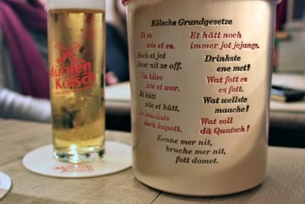 Foto: Ein Glas Kölsch und daneben ein steinerner Krug mit eingravierten kölschen Weisheiten, dem "Kölschen Grundgesetz" mit Punkten wie "Et hätt noch immer jot jejangen"