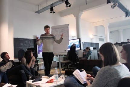 Foto: Ein junger Mann steht gestikulierend vor einem Flipchart und redet mit den aROund-Redakteuren.