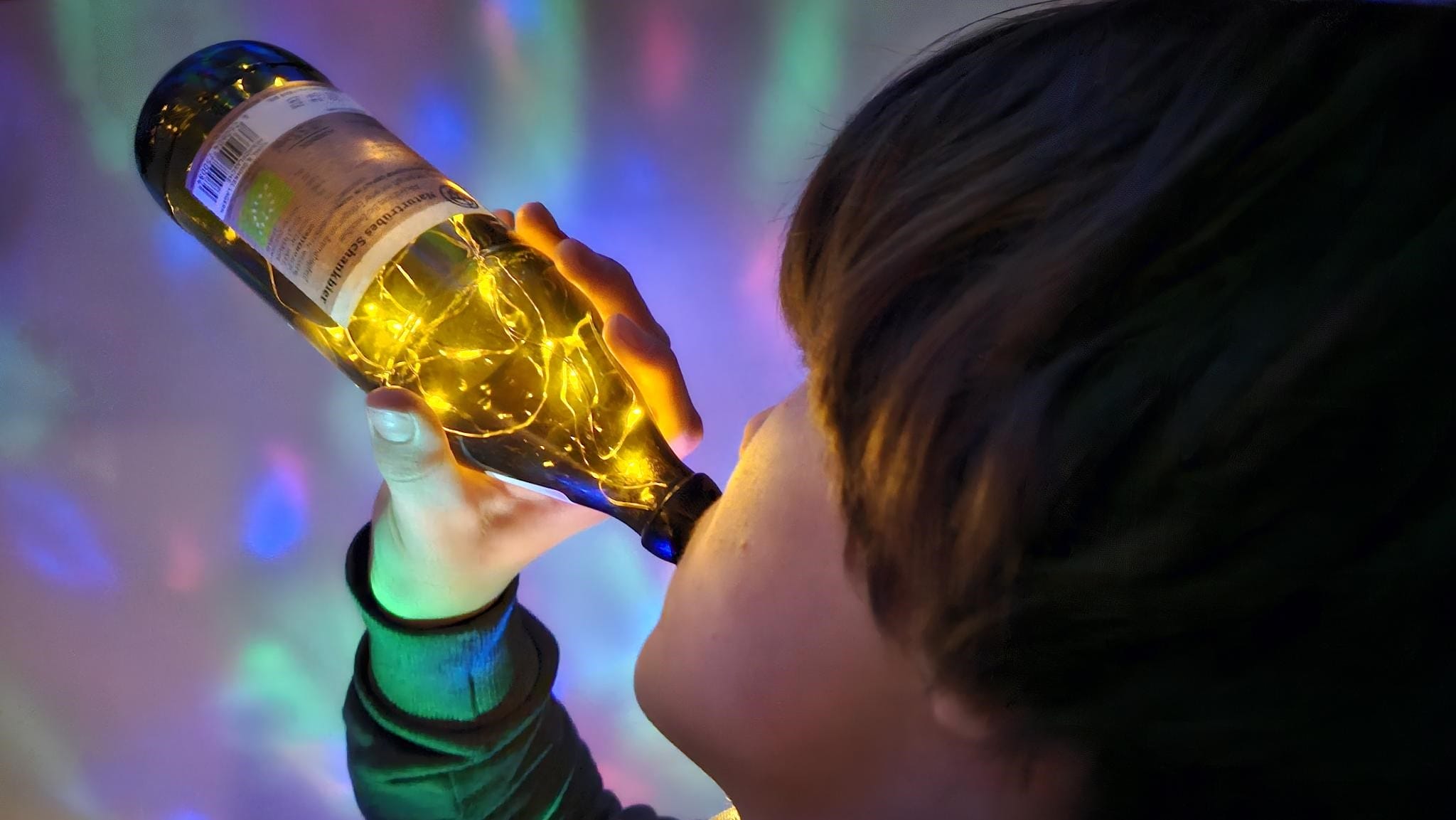 Foto von einem Teenager, der aus einer Bierflasche trinkt, in der kleine LED Lichter leuchten.