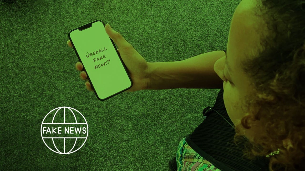 Foto: Eine junge Frau schaut auf ihr Handy, worauf die Frage: "Überall Fake News?" zu lesen ist.