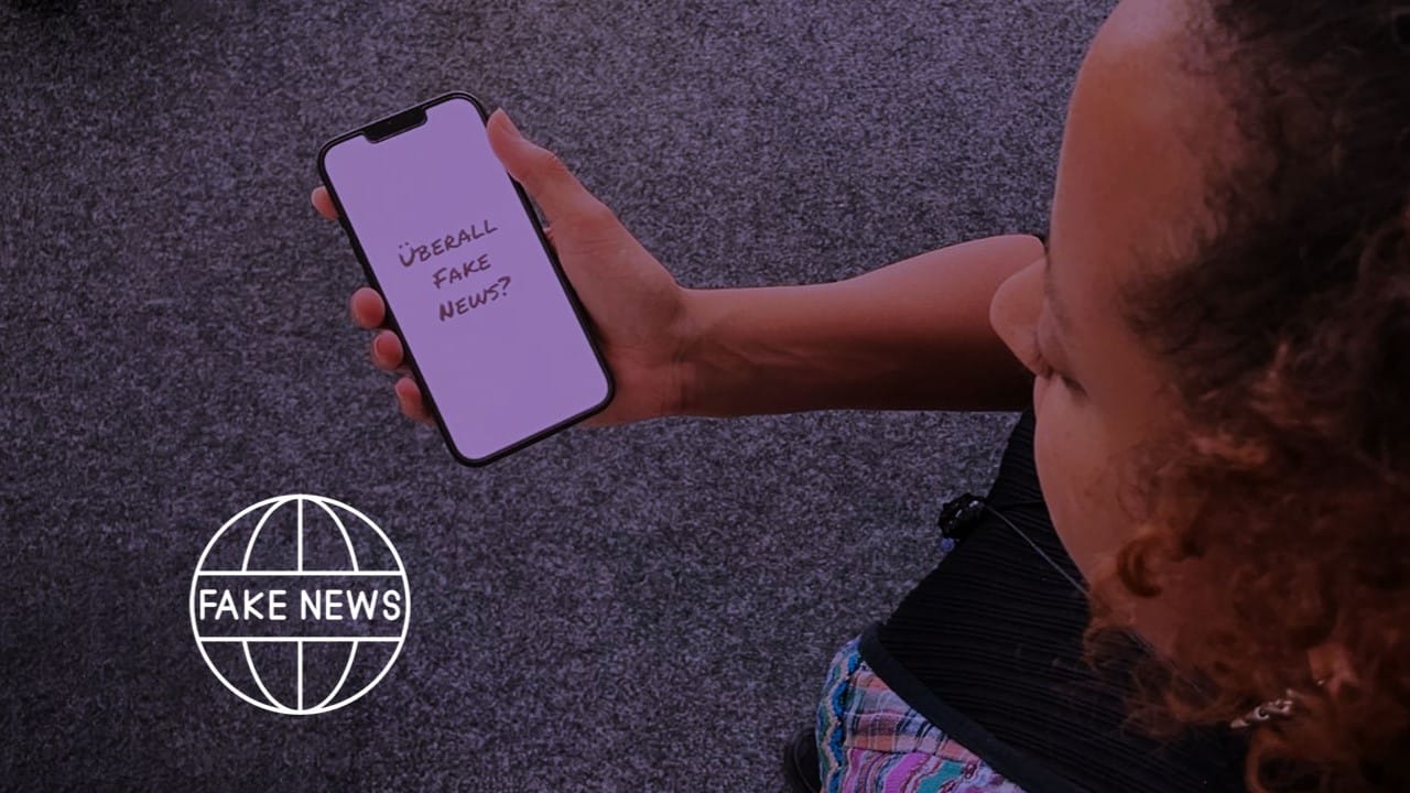 Foto: Eine junge Frau hält ein Smartphone in der Hand, auf dessen Bildschirm die Frage steht: "Überall Fake News?"