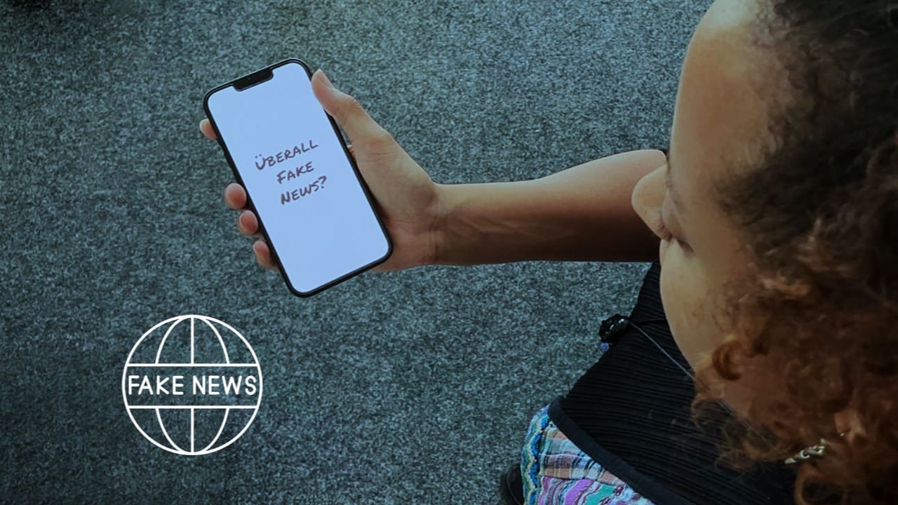 Foto: Eine junge Frau schaut auf ihr Handy, worauf die Frage: "Überall Fake News?" zu lesen ist.