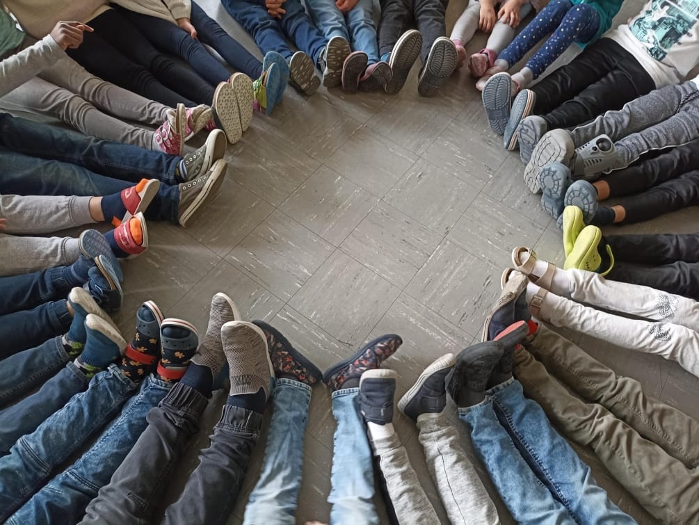 Man sieht die Füßer aller Kinder der Klasse 3b , die in einem Kreis auf dem Boden sitzen