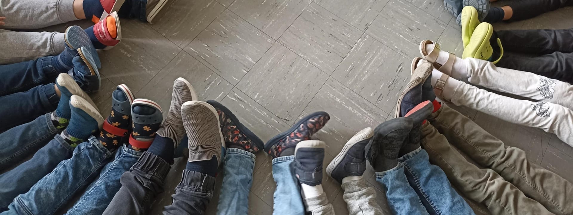 Foto: Viele Beine von Kindern, die in einem Halbkreis sitzen und Hausschuhe tragen
