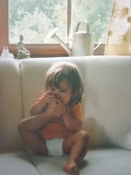 Hannah als Kleinkind mit eigenem Fuß im Gesicht.