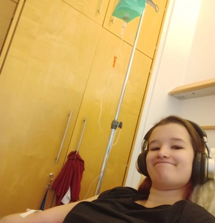 Selfie Hannah im Krankenhaus mit Kopfhörerern auf und Infusion im Arm
