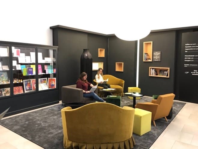 Foto: Ein Raum, eingerichtet wie eine Lounge, mit Bücherregalen. Zwei junge Frauen sitzen dort in Sesseln und lesen.