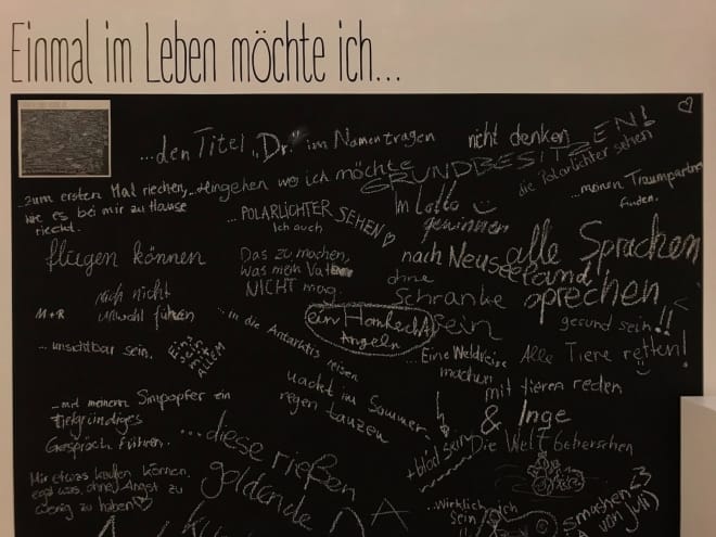 Foto: Eine schwarze Tafel mit der Überschrift "Einmal im Leben möchte ich..." auf die mit Kreide verschiedene Vervollständigungen des Satzes geschrieben wurden.