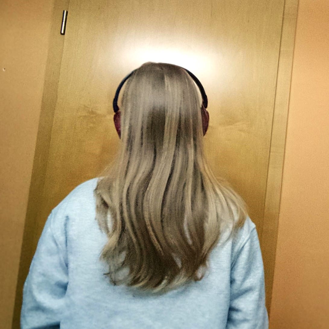 Foto: Eine Jugendliche mit langen blonden Haaren und roten Kopfhörern auf den Ohren - man sieht sie nur von hinten