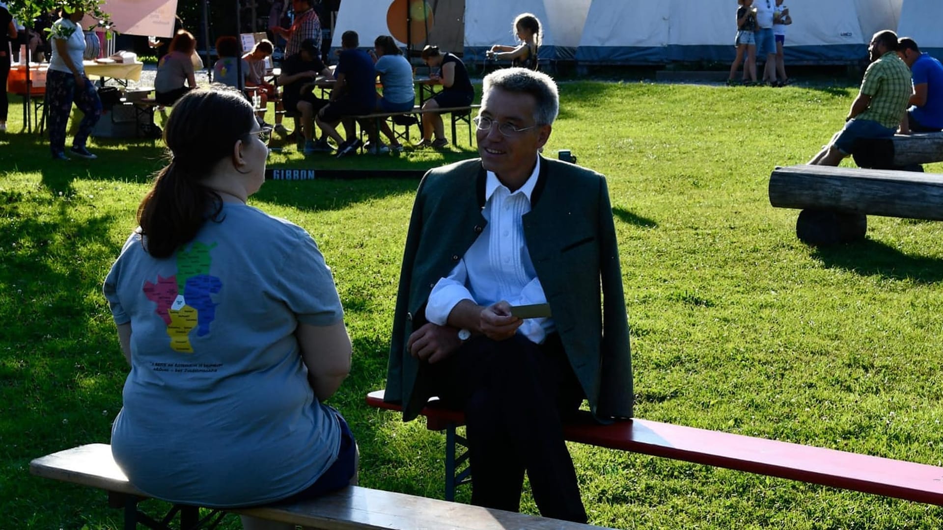 Der Landrat interviewt Melina. Beide sitzen sich auf Bierbänken gegenüber. Melina trägt ein aROund T-Shirt. Im Hintergrund sieht man viele Jugendliche.
