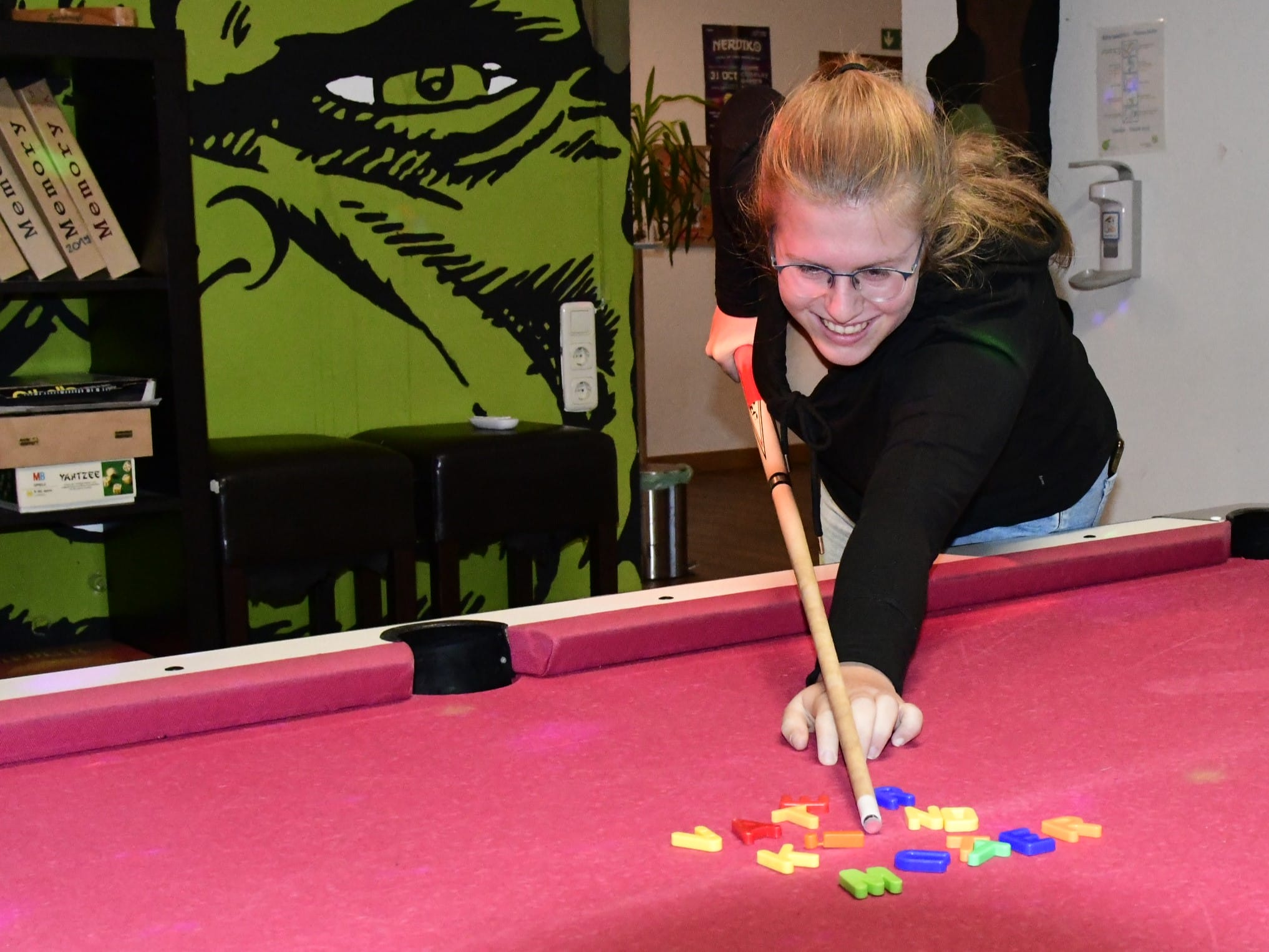 Foto: Eine Jugendliche hat Spaß daran, mit einem Billard-Queue Magnetbuchstaden durcheinanderzustoßen, die die Worte Vater, Mutter, Kind gebildet hatten