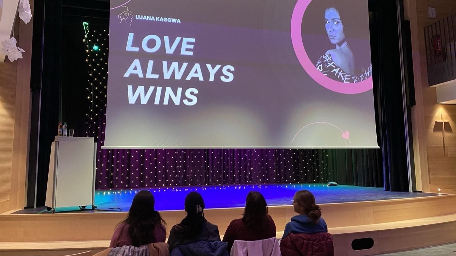 Foto: Vier Personen sitzen vor Beginn des Vortrags vor der Bühne in der ersten Reihe