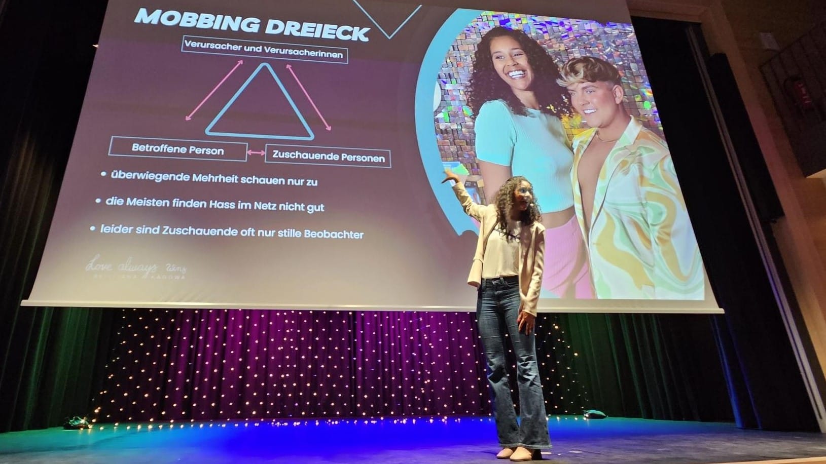 Foto: Lijana auf der Bühne vor der einem Foto von ihr mit Twenty4Tim und einer Grafik des Mobbing-Dreiecks