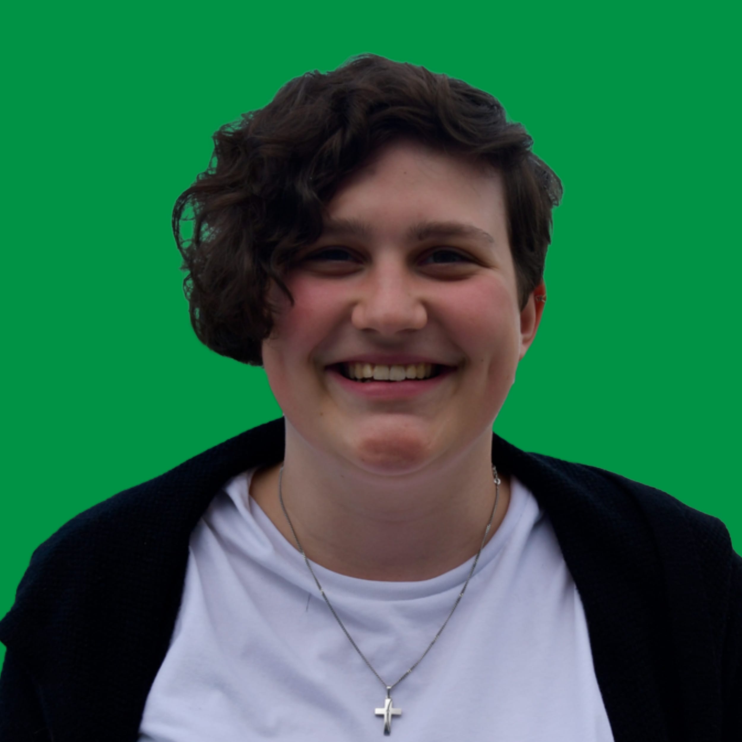 Eine junge Frau mit einer Kurzhaarfrisur und einem kleinen silbernen Kreuz an einer Kette schaut fröhlich in die Kamera