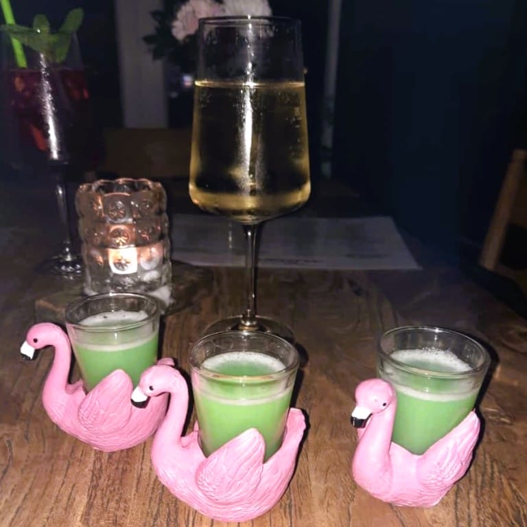 Foto: Gläser mit leuchtend grünen Drinks stecken in Plastik-Halterungen, die aussehen wie rosa Schwäne