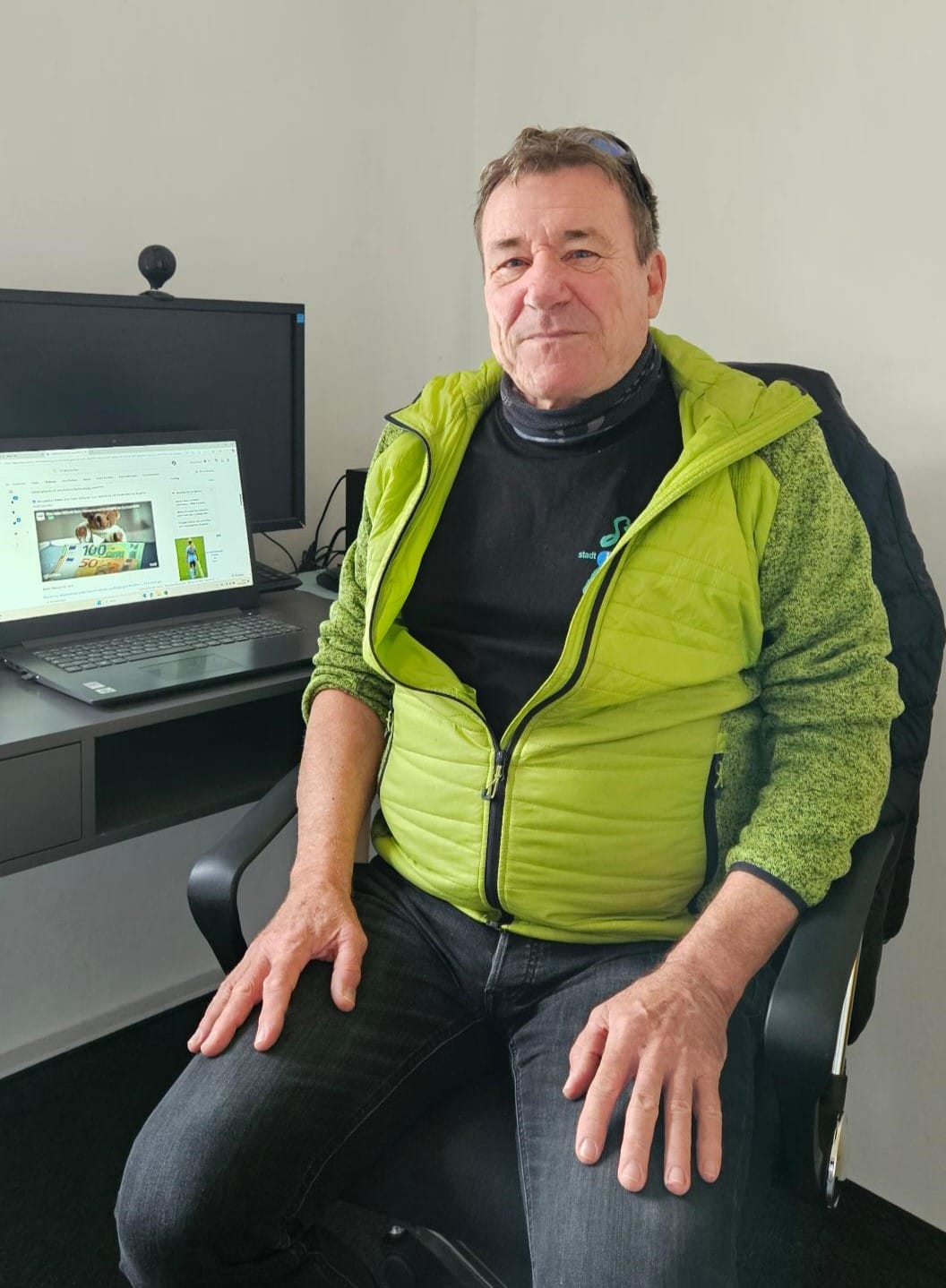 Foto: Ein Mann sitzt auf einem Bürostuhl vor einem Notebook und schaut freundlich in die Kamera