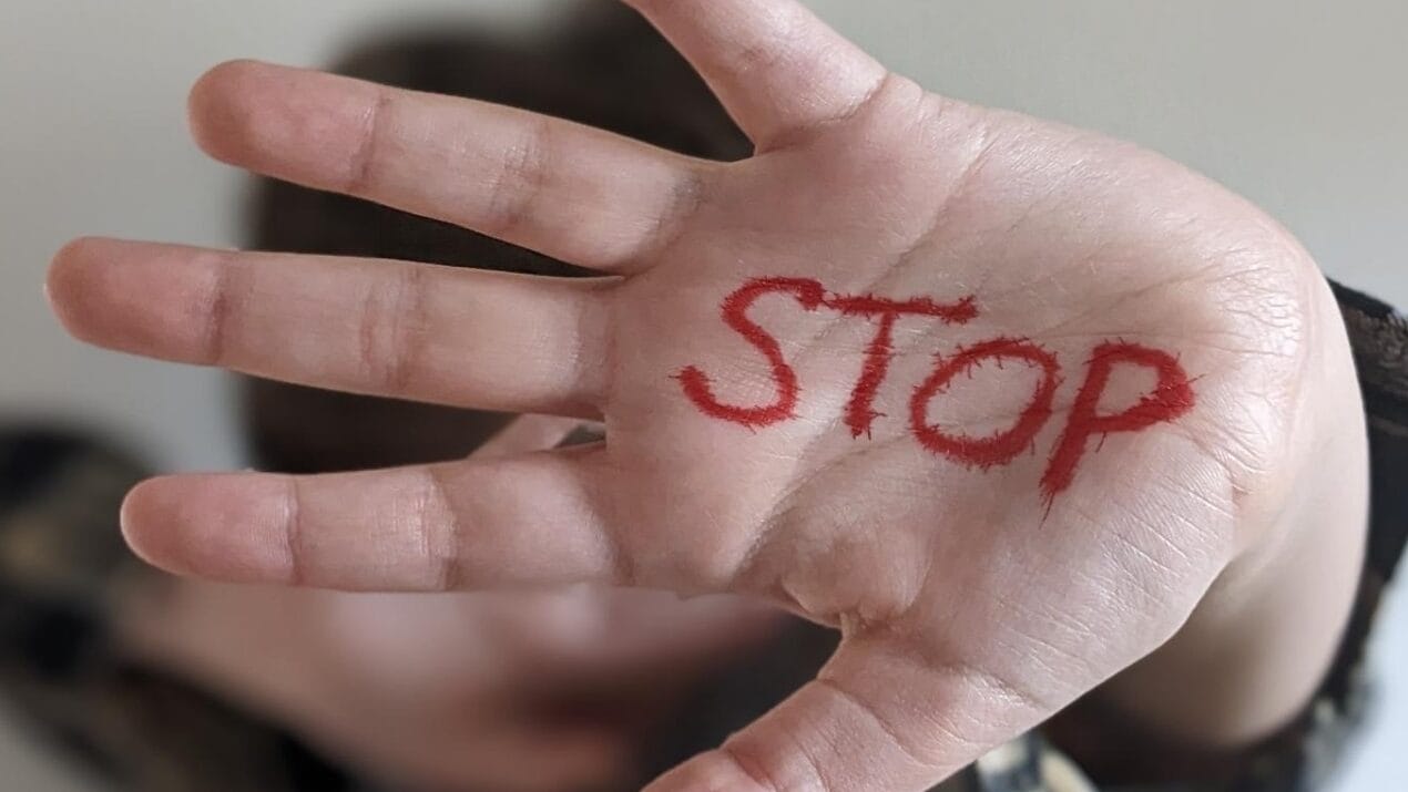 Foto: Auf einer abwehrend ausgestrecken Hand steht in roten Großbuchstaben das Wort STOP