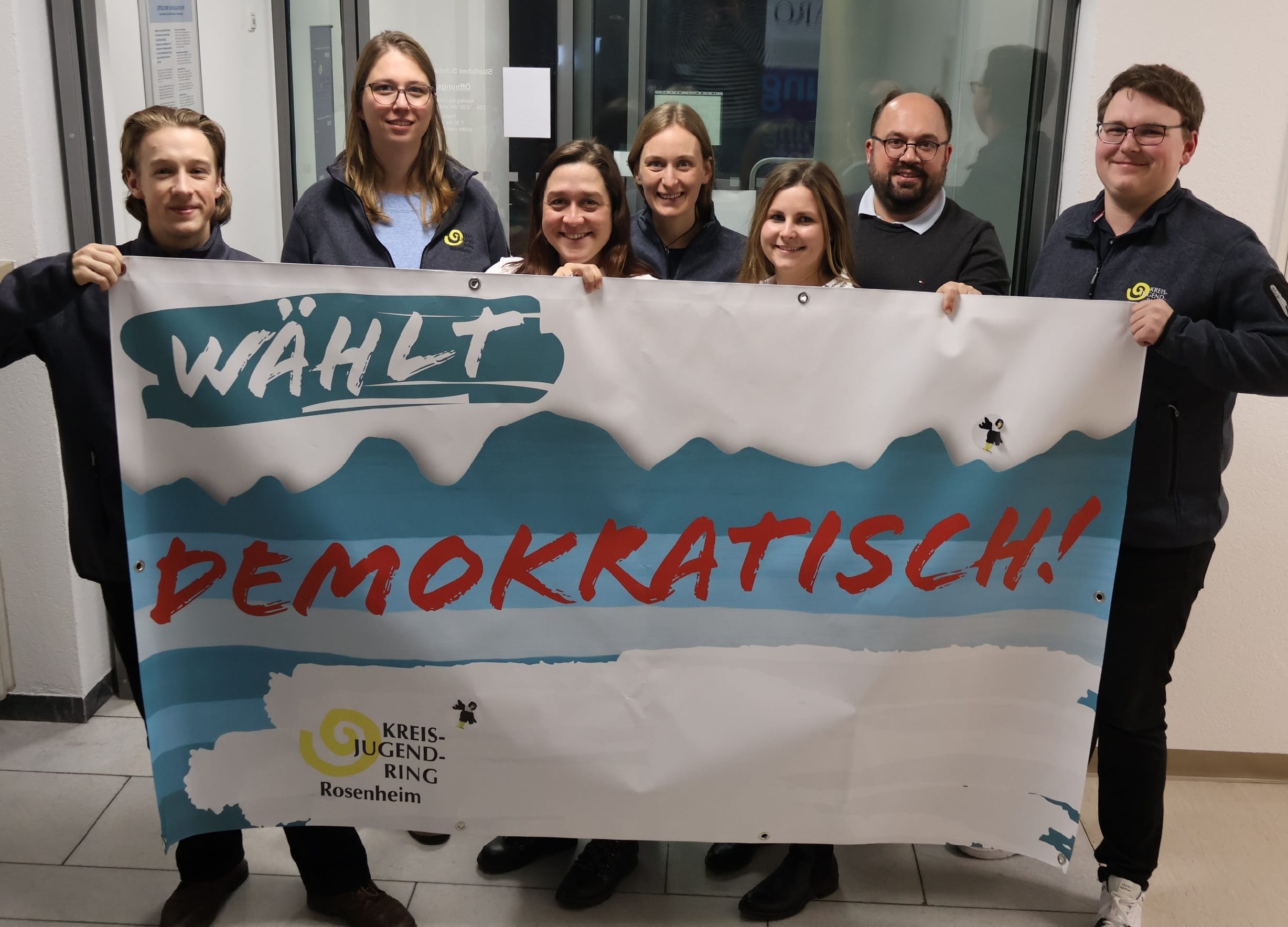 Foto: Sieben Personen halten ein großes Banner in die Kamera. Darauf steht "Wähl demoktaisch!" und das Logo des Kreisjugendrins Rosenheim