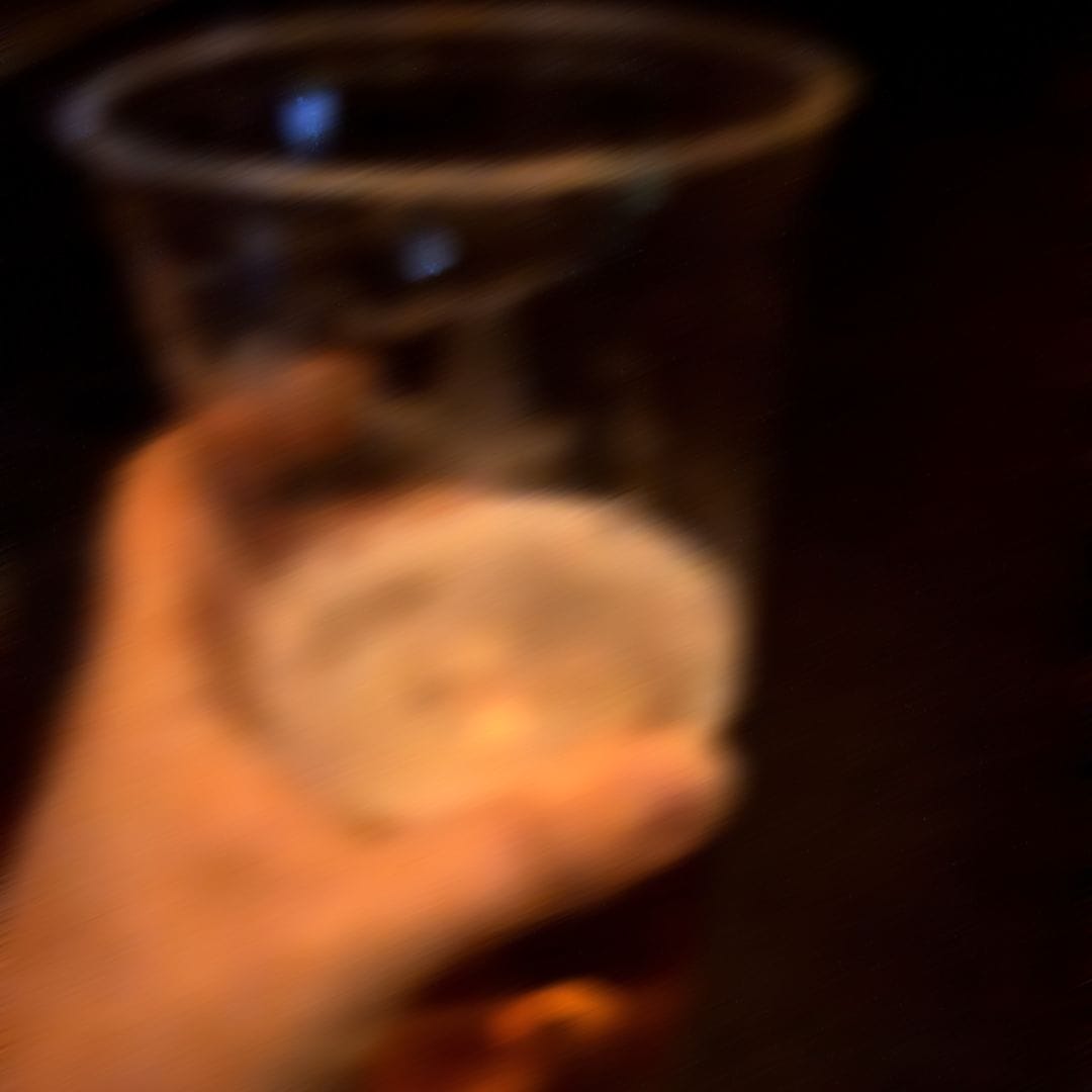 Sehr unscharfes Foto / Blick auf die eigene Hand, die einen Becher voll Bier hält